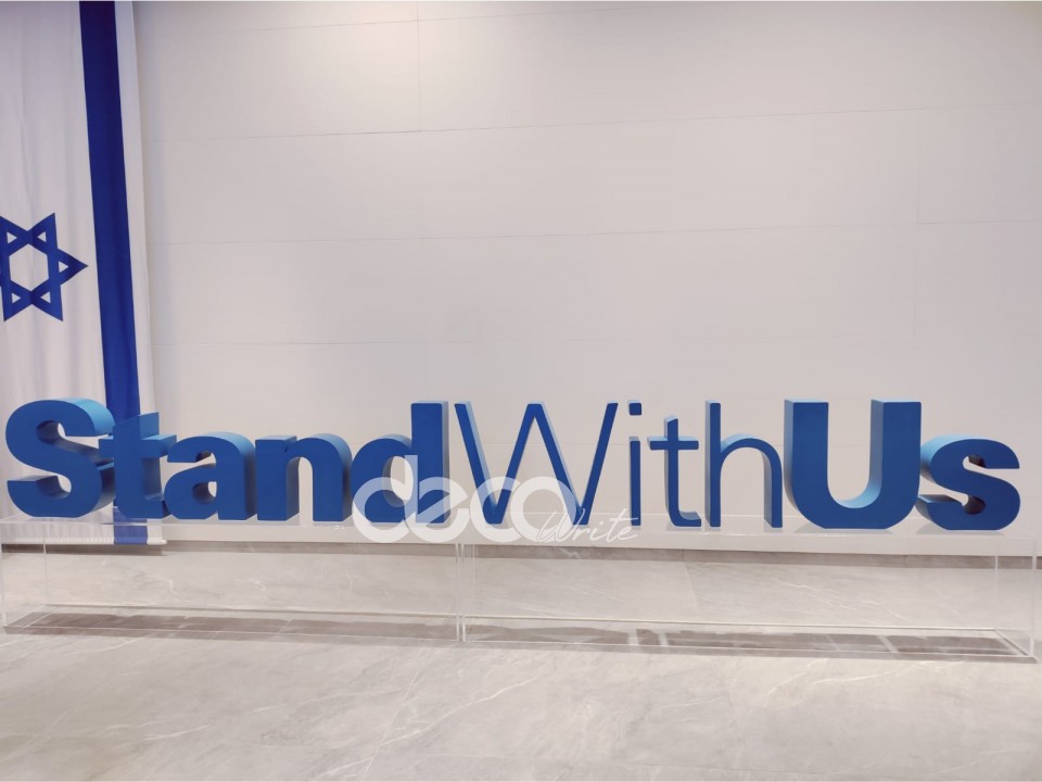 לוגו למוזאון STAND WITH US בנוי על במה מפרספקס שקוף